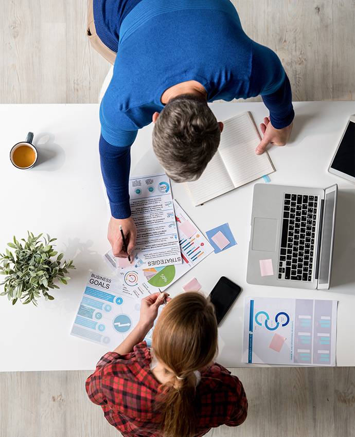 Mann und Frau am Arbeitsplatz mit Laptop und diversen Unterlagen